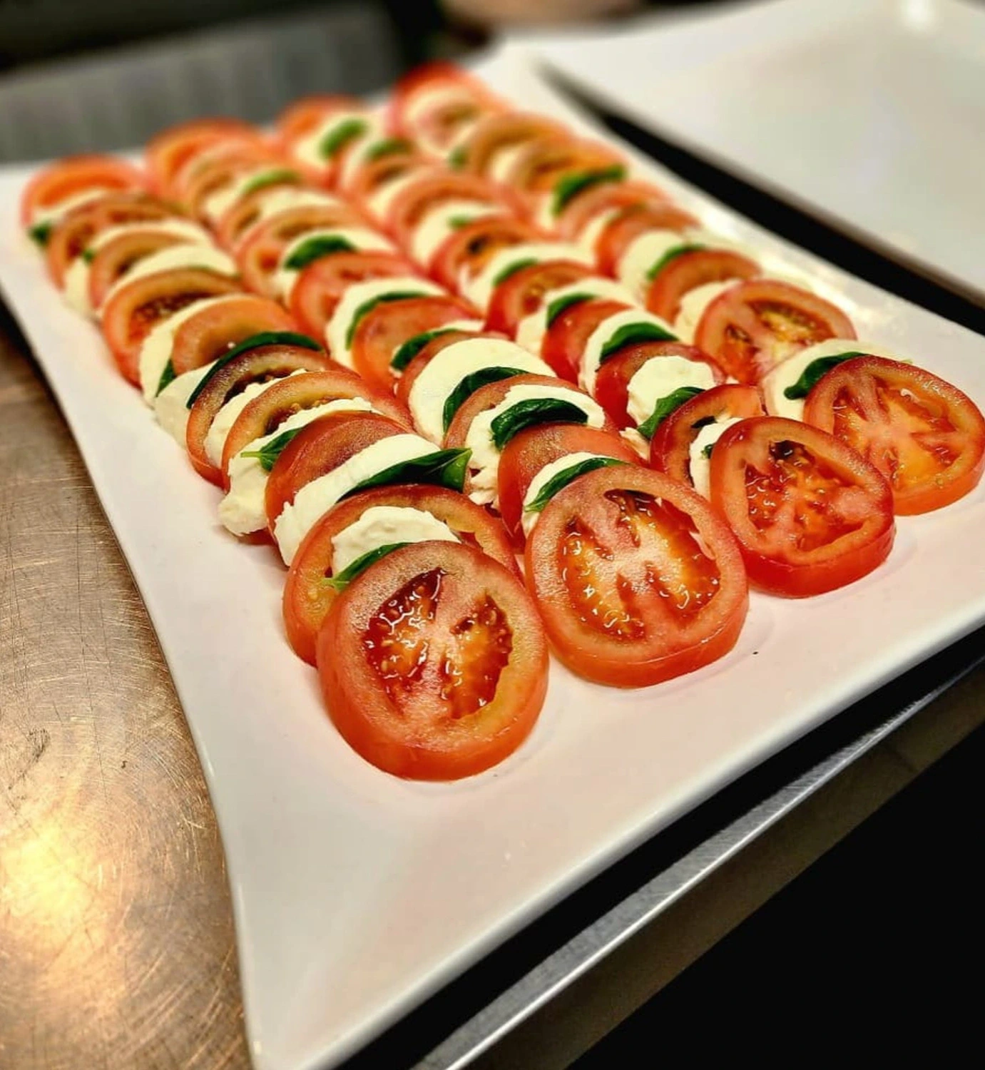Caprese in dichten parallelen Reihen aus Tomate, Mozzarella und Basilikum auf einer langen weißen Platte
