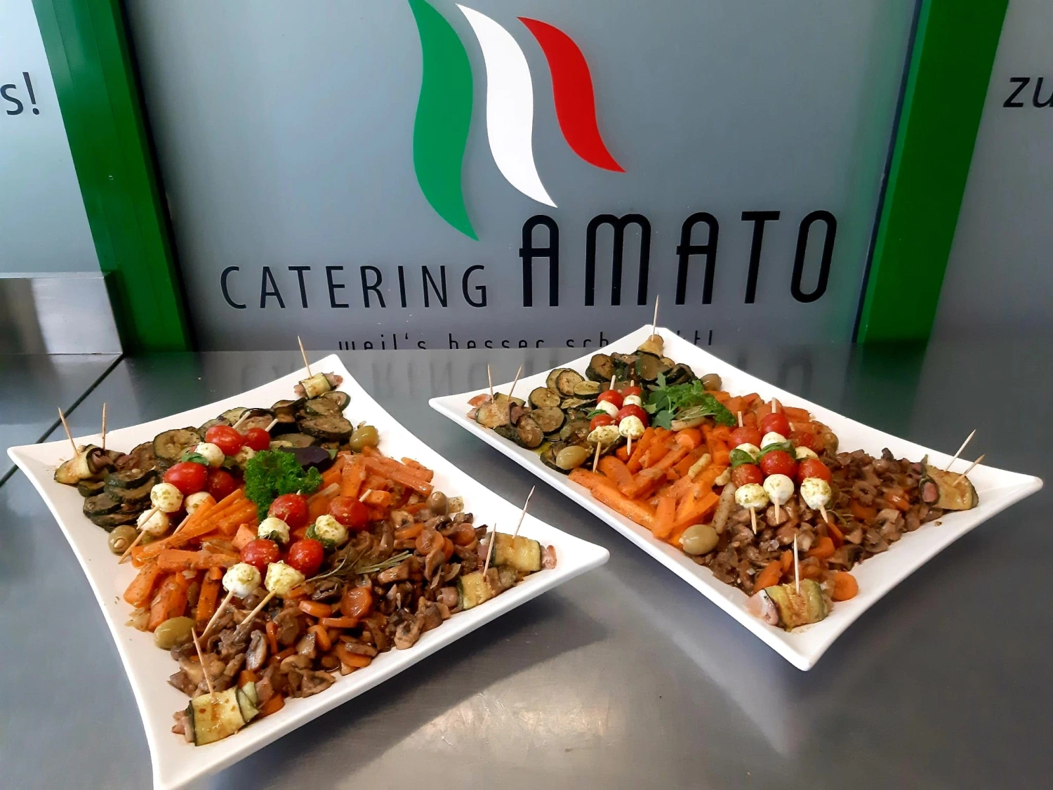 Zwei Antipasti-Platten mit gegrillter Zucchini, Aubergine, Karotten, marinierten Champignons und Mozzarella-Tomaten-Spießen vor der Markenwand von Catering Amato