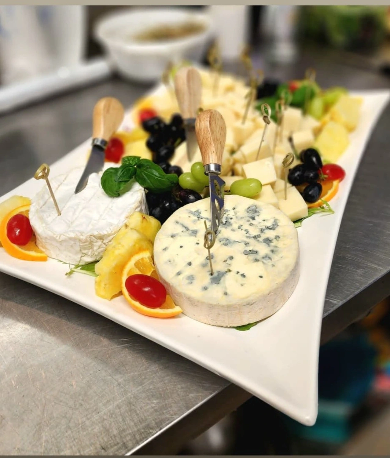Käse- und Obstplatte mit Brie, Blauschimmelkäse, Trauben, Ananas und Käsemessern mit Holzgriff